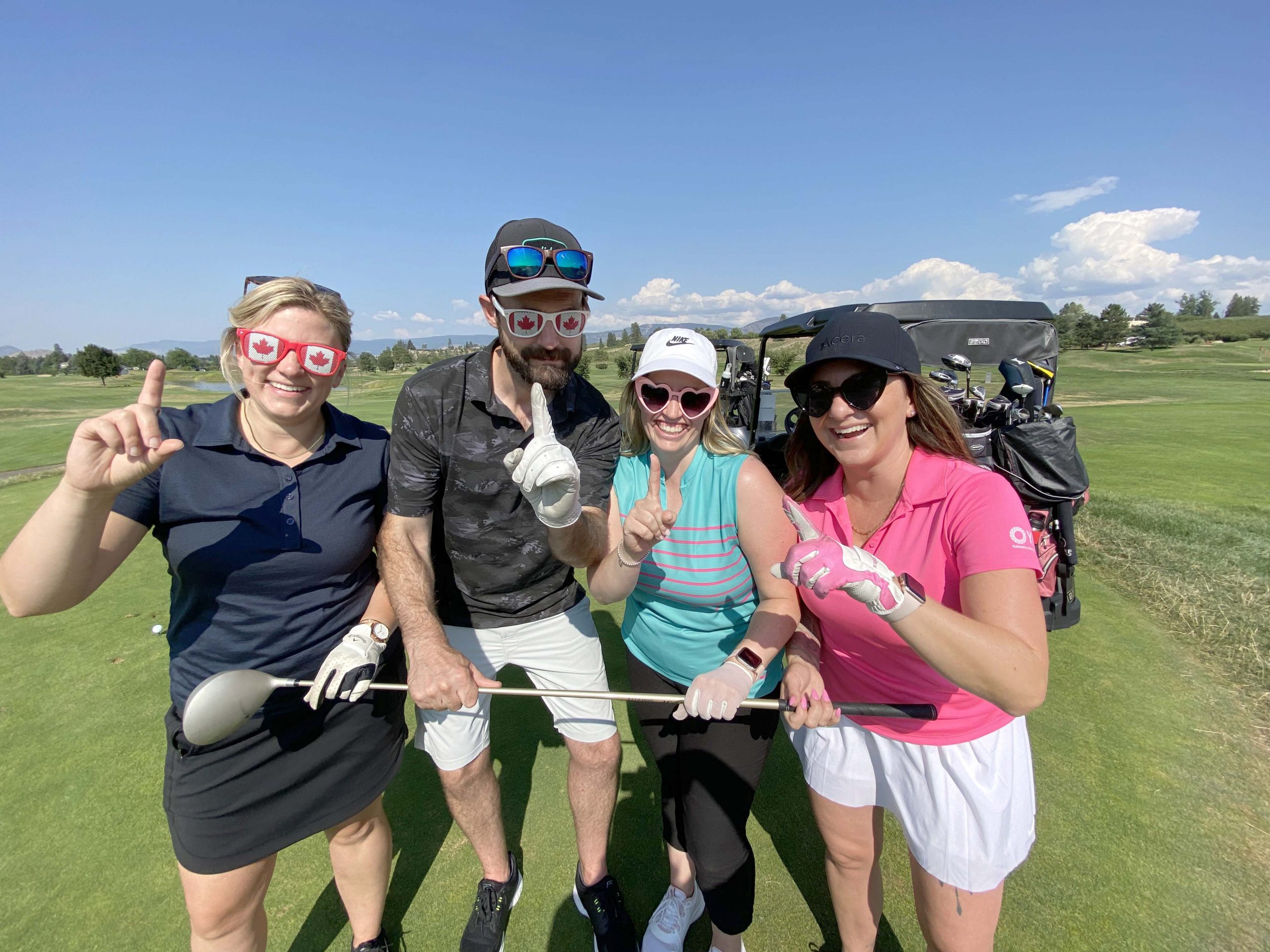 A golfing foursome lined up next to eachother, each holding up their index finger signifying number one.